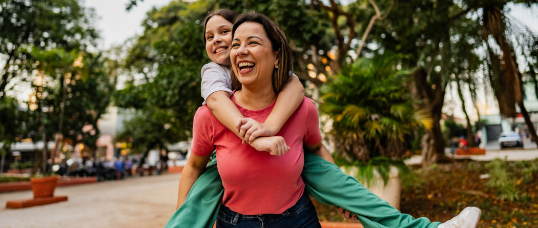 A woman giving a child a piggy back ride in a park 