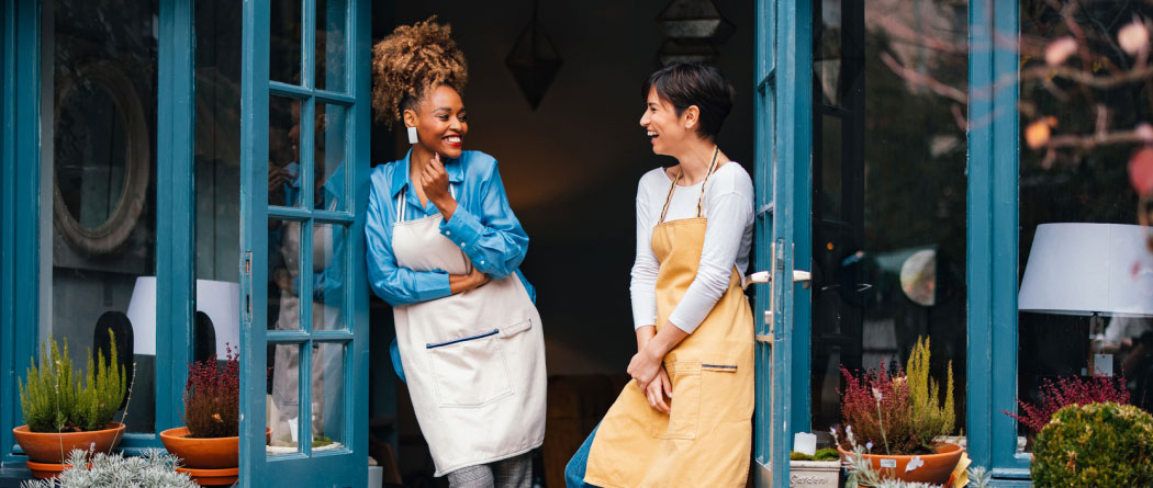 Two women in aprons standing outside a shop